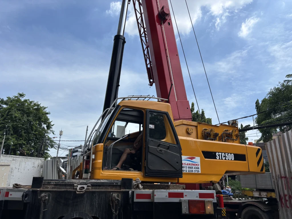 Operator crane berAPD lengkap melakukan pre-shift inspection mobile crane sebelum beroperasi